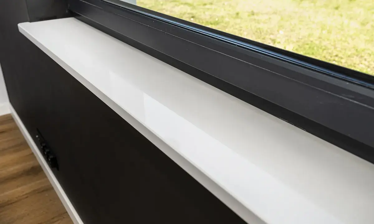 Biały parapet z materiału imitującego marmur, nazwa tego tworzywa to konglomerat kwarcowy.
