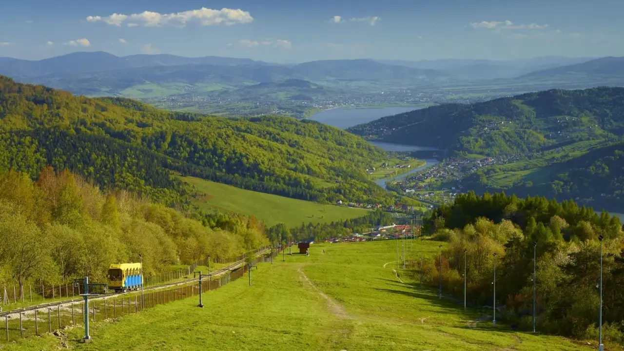 Widok na zielone beskid mały szczyty, jezioro i miasteczko. Kolejka krzesełkowa wjeżdża na górę.