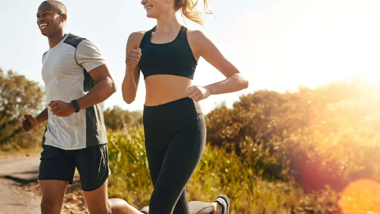 Ein Mann und eine Frau joggen lachend auf einem Feldweg. Die Sonne scheint, und die Atmung beim Joggen ist gleichmäßig und tief.