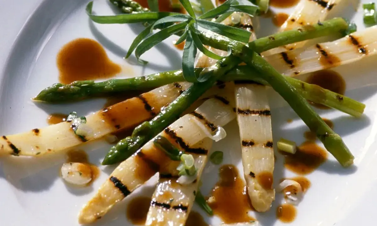 Gegrillter Spargel auf einem Teller, mit einer würzigen Sauce beträufelt und garniert mit frischen Kräutern.