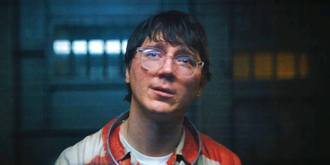 Paul Dano med glasögon och blodfläckar på sin randiga skjorta, i en mörk miljö med ljus bakom.