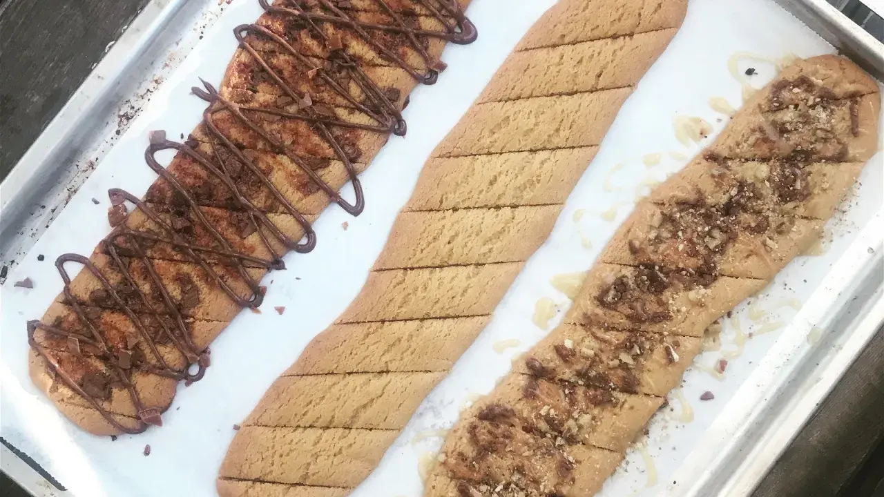 Tre långa, avlånga kakor på en plåt. En är dekorerad med chokladglasyr och hackad choklad, en annan med strössel och en tredje med honung och nötter. Perfekt för ett kolakakor recept!