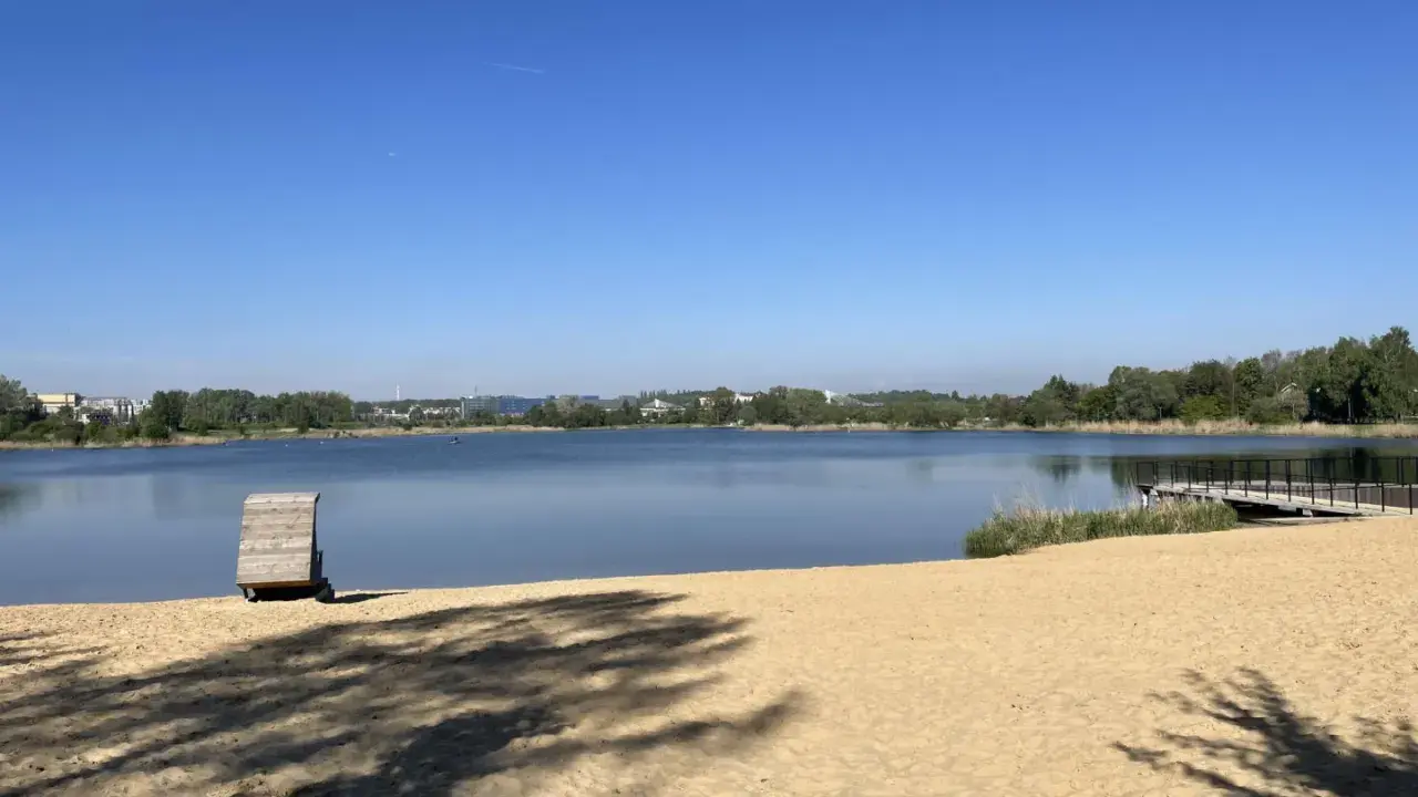 Plaża bagry z drewnianą przebieralnią i pomostem, w tle jezioro i zieleń.