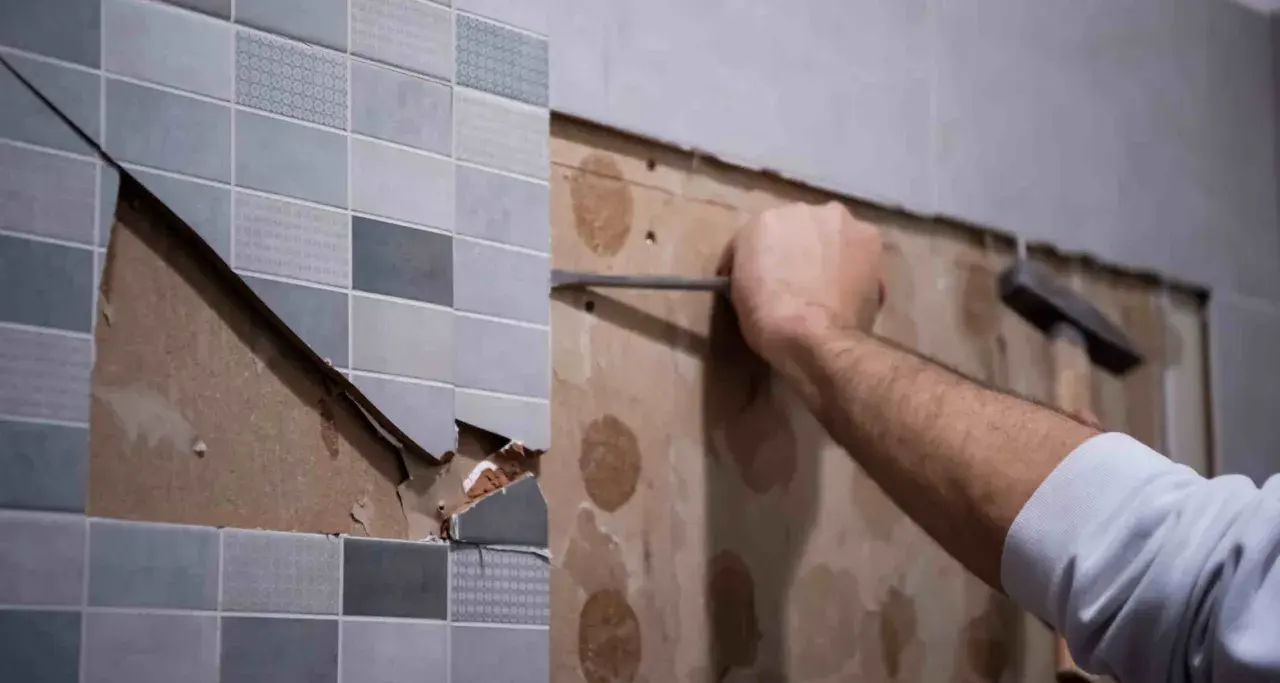 Persona usando una espátula para quitar azulejos de una pared.
