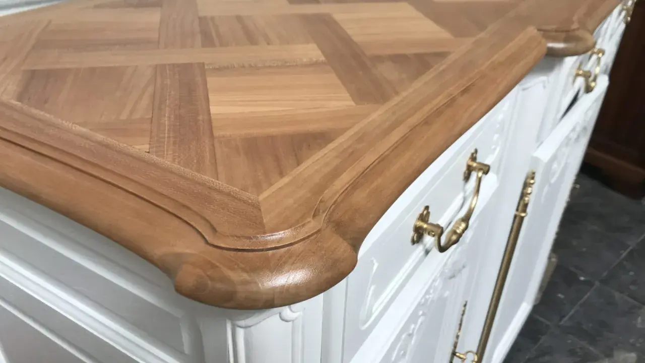 Un meuble ancien relooké en moderne, avec un plateau en bois clair à motif géométrique et des poignées dorées sur un corps blanc.