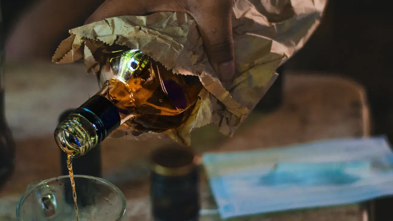 Ręka trzyma butelkę z alkoholem, z której nalewany jest płyn do szklanki. To może być początek drogi do dawki śmiertelnej alkoholu.