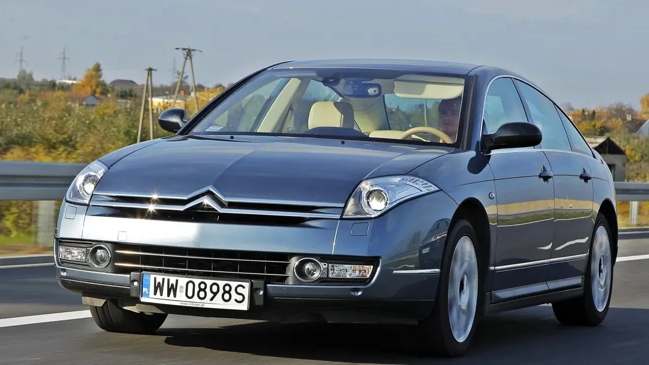 Elegancki Citroën C6 w kolorze granatowym jedzie po drodze. Wnętrze z jasną tapicerką i kierowcą.