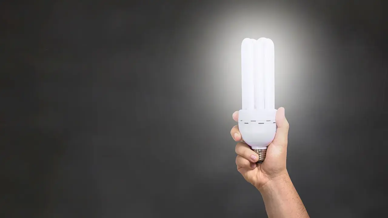 Dłoń trzymająca energooszczędną żarówkę o mocy 806 lumenów, rozświetlającą ciemne tło.