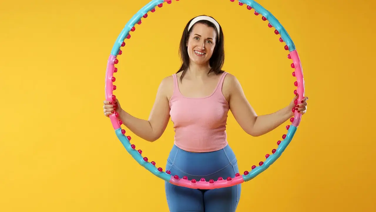 Uśmiechnięta kobieta z hula hop. Dowiedz się, jak dobrać hula hop do wzrostu, by ćwiczenia były efektywne i przyjemne.