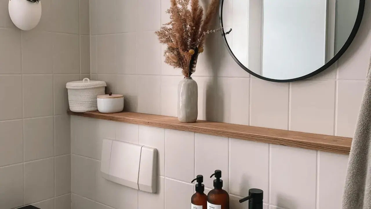 Étagère en bois dans une salle de bain carrelée, avec des décorations et un miroir rond.