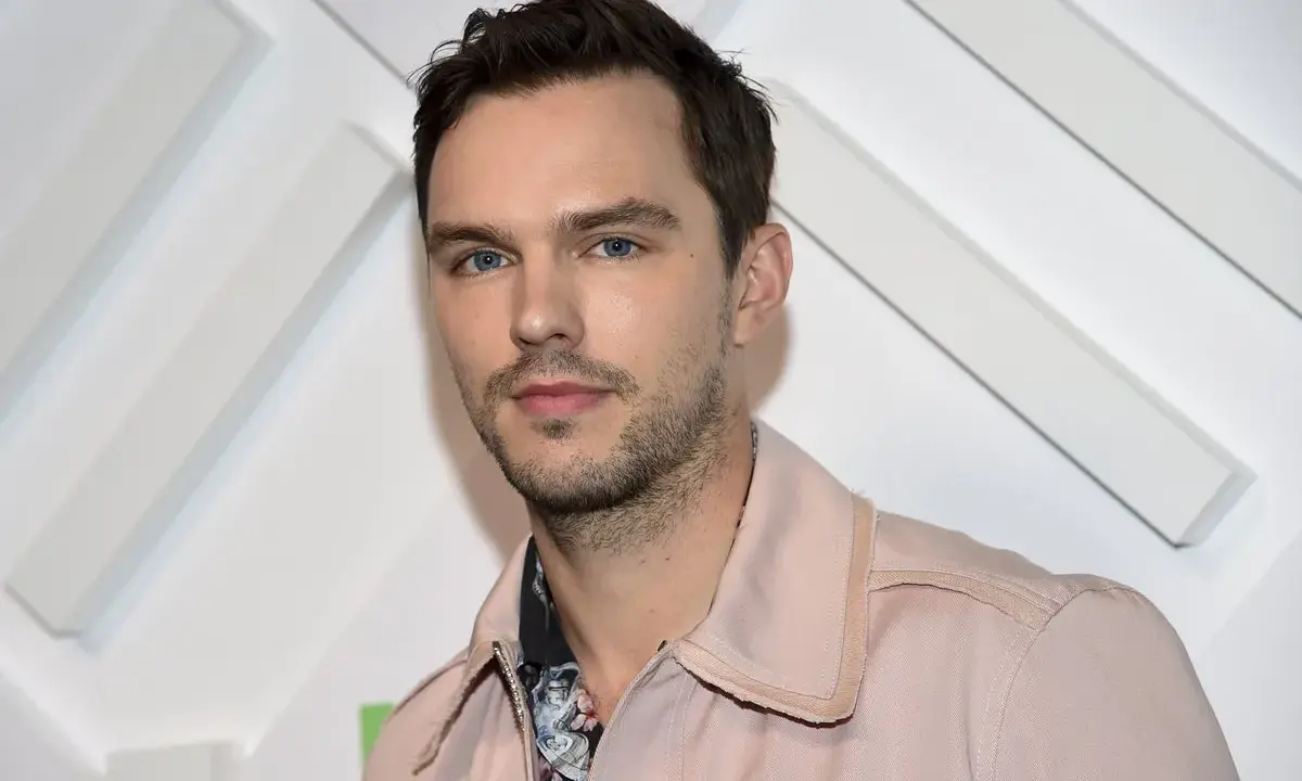 Nicholas Hoult, känd från filmer och tv-program, poserar framför en vit bakgrund med diagonala linjer.