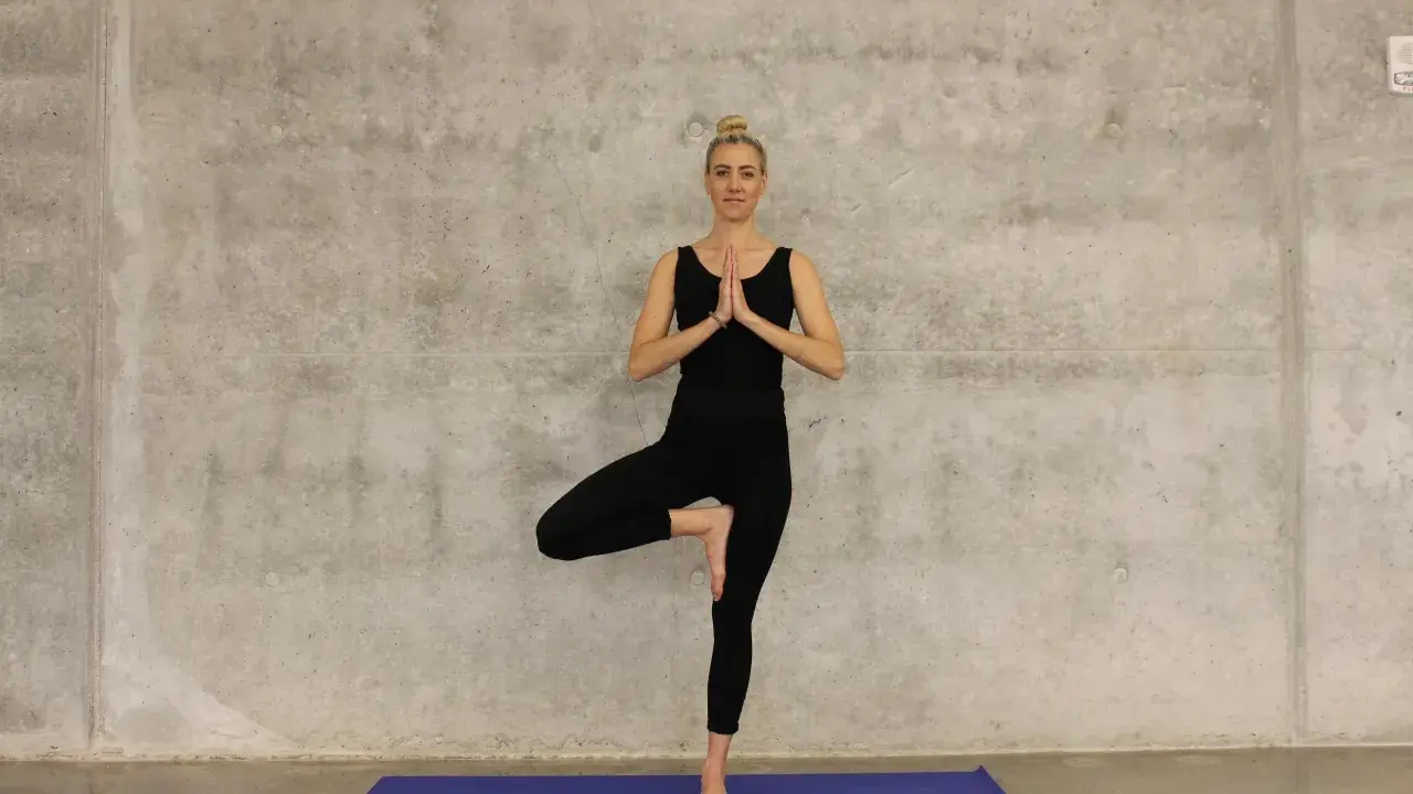 Kvinna i svart träningsklädsel utför trädpositionen, en klassisk yogaövning som passar utmärkt för senior yoga.