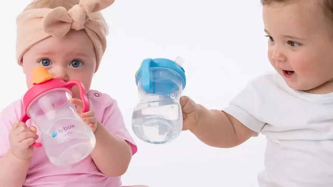 Dzieci z zaciekawieniem patrzą na swoje pierwsze butelki do picia wody. Jedno dziecko trzyma różową, drugie niebieską.