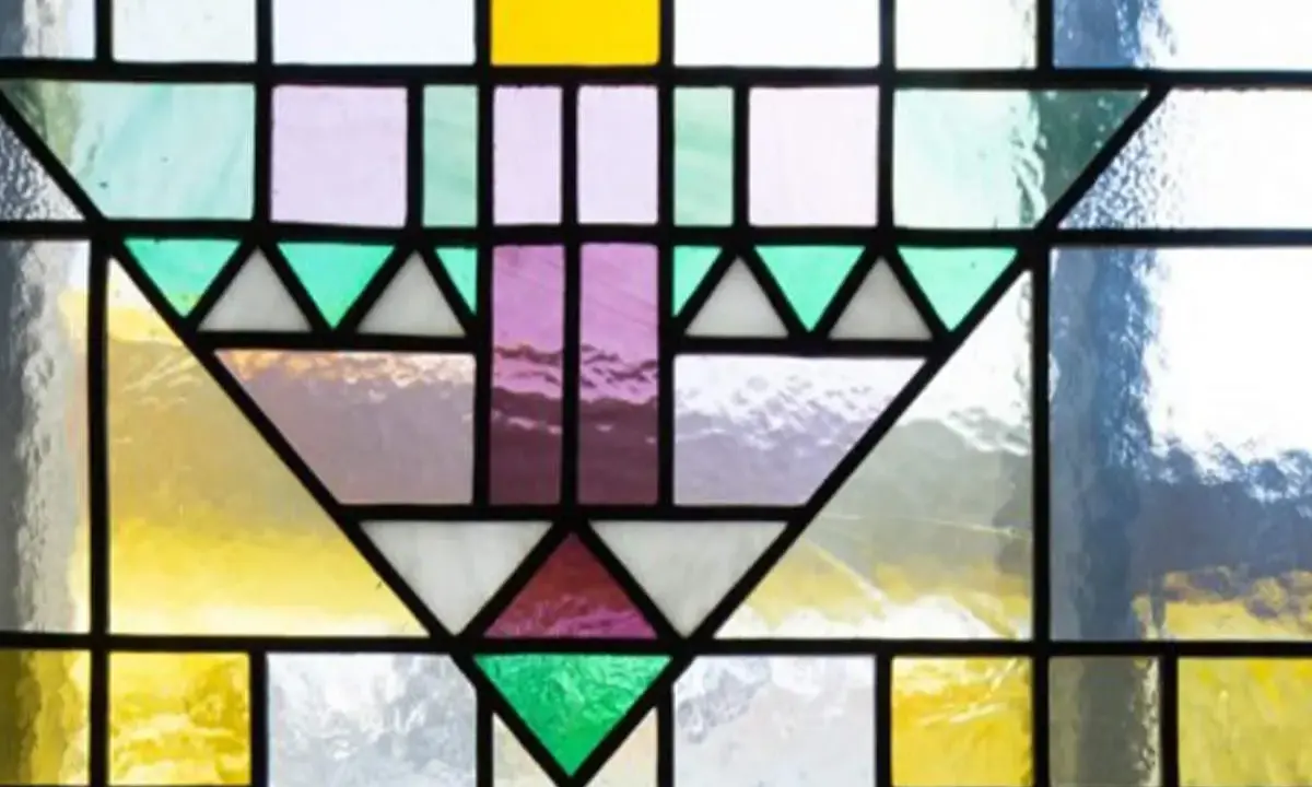 Un motif géométrique coloré orne cette fenêtre vitraux, mêlant le jaune vif, le violet doux et le vert émeraude.
