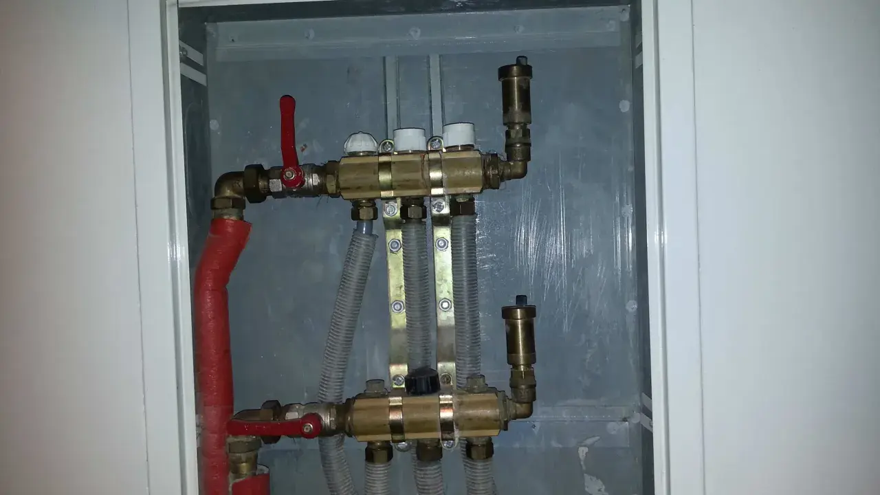 Widoczny zawór RTL na powrocie systemu ogrzewania podłogowego. Metalowa obudowa skrywa skomplikowaną instalację hydrauliczną.