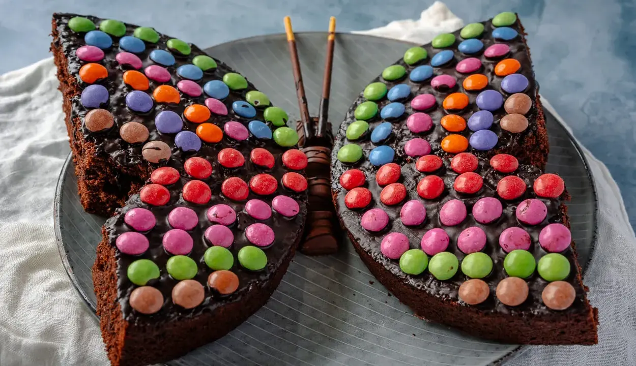 Ein schokoladiger Smarties Kuchen in Form eines Schmetterlings, der mit bunten Smarties dekoriert ist.