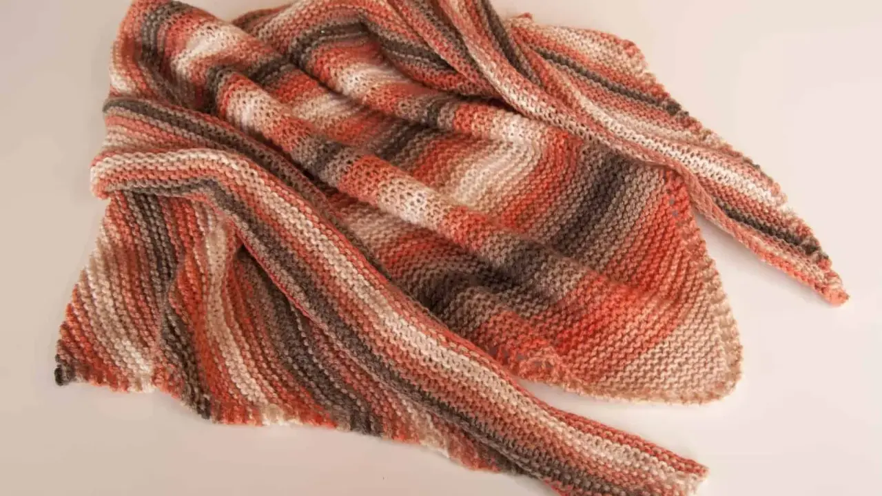 Chal dos agujas tejido a mano con rayas degradadas en tonos naranjas, marrones y blancos. Suave y acogedor, perfecto para cualquier ocasión.