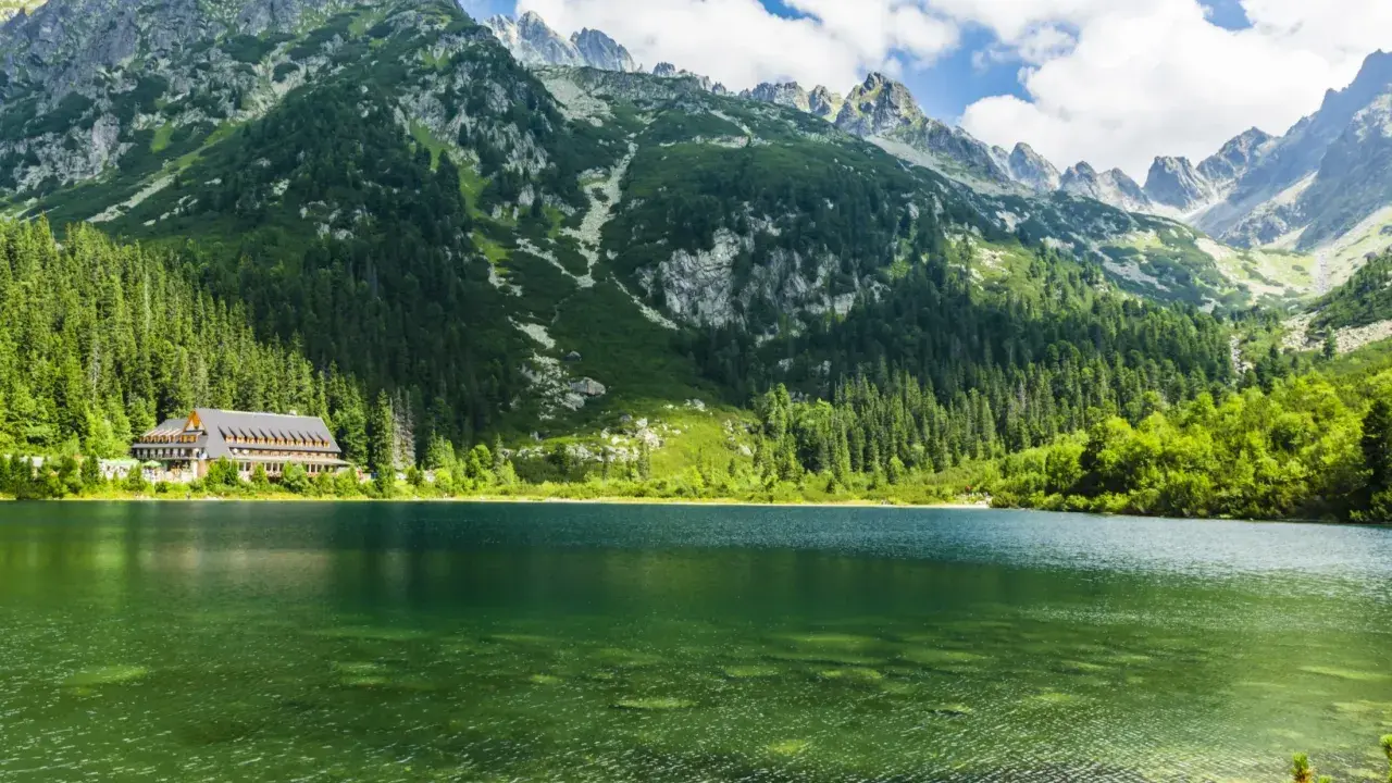 Malownicze Tatry Morskie Oko z krystalicznie czystą wodą, otoczone zielonymi lasami i skalistymi szczytami.