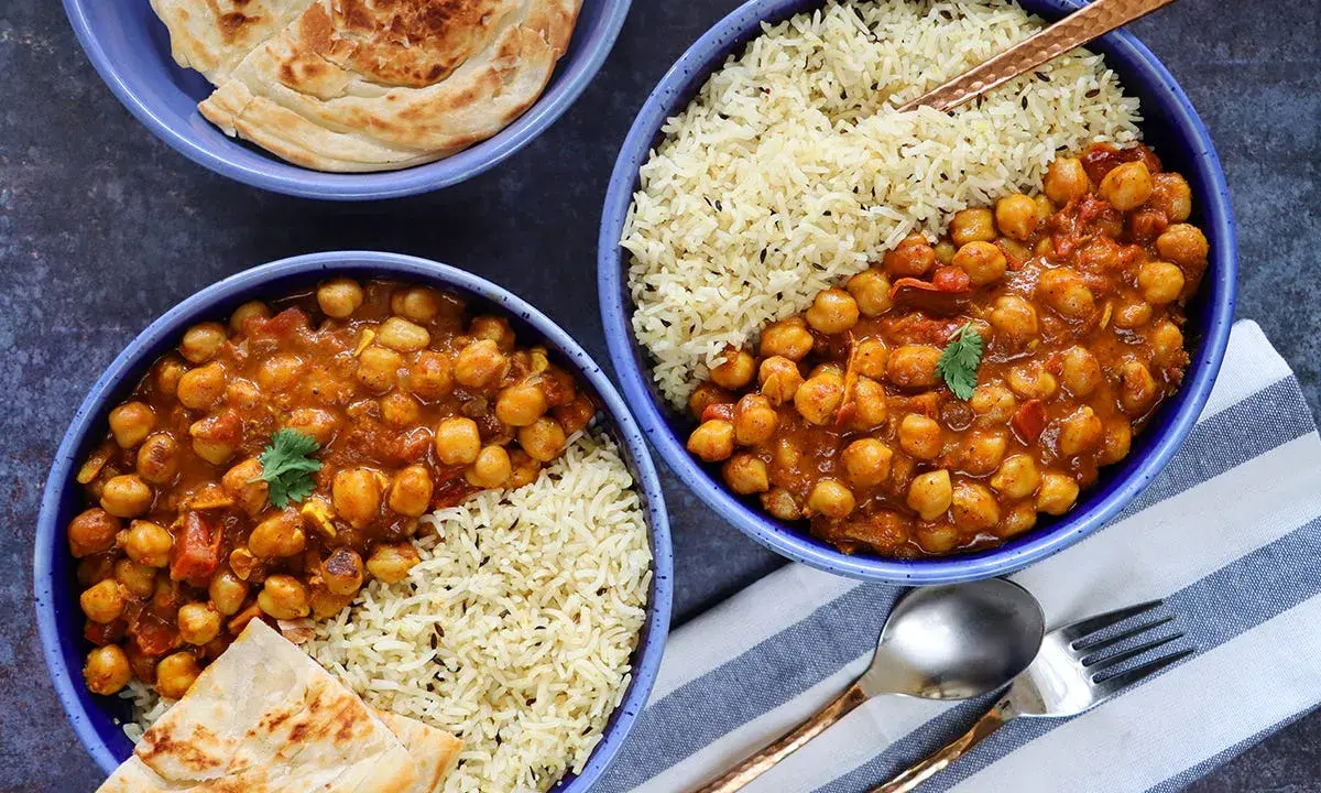 Dos tazones de curry de garbanzos con arroz basmati y pan naan.