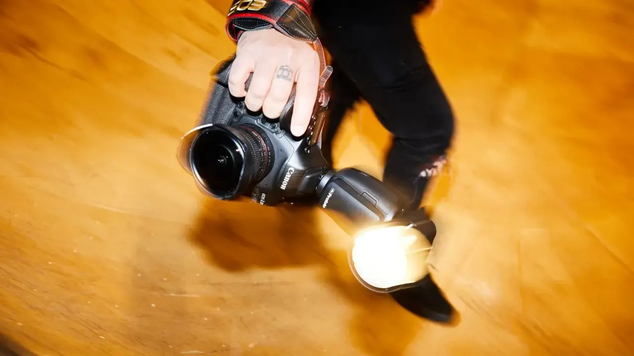Dłoń fotografa trzyma aparat z lampą błyskową. Długi czas naświetlania tworzy efekt ruchu.