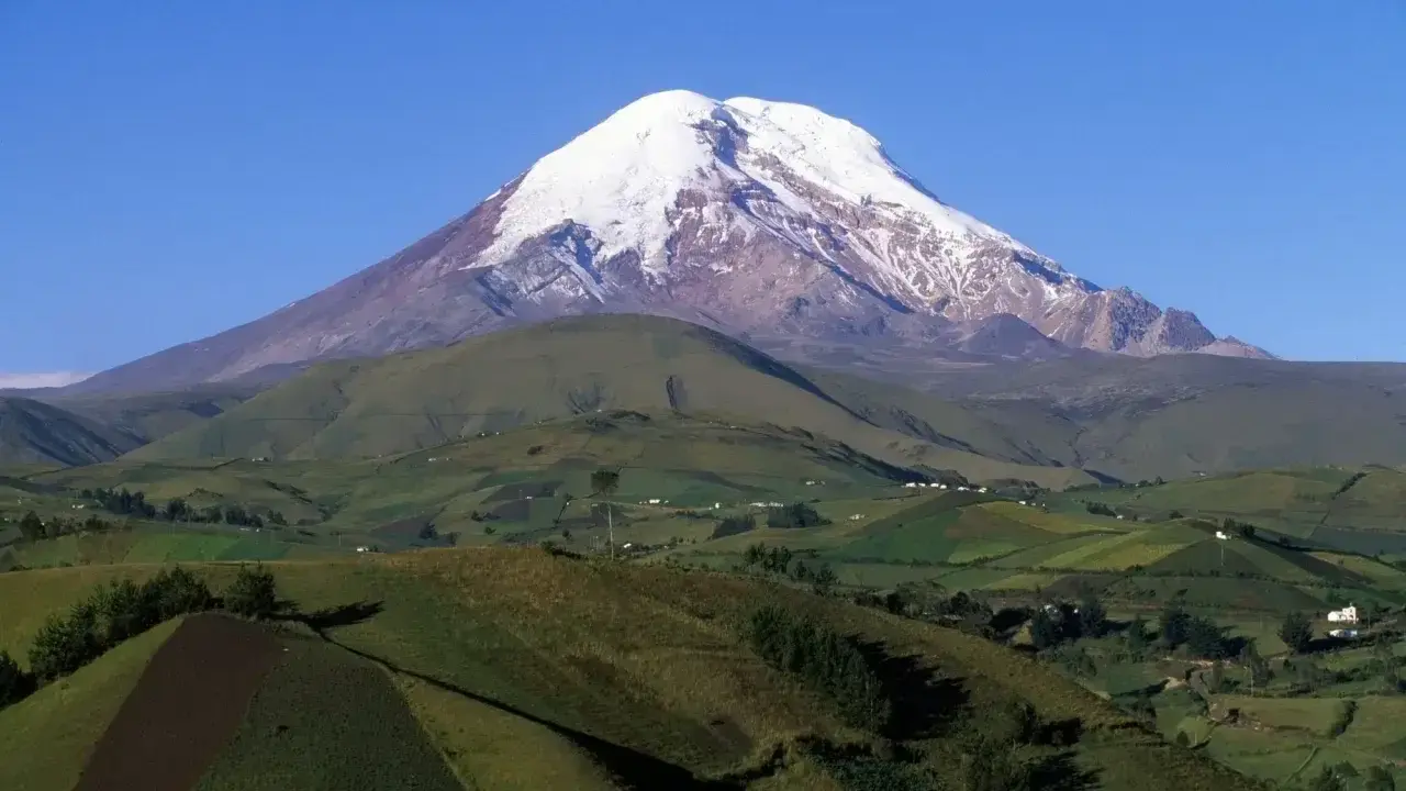 Ośnieżony wulkan Chimborazo, najwyższy punkt na ziemi, góruje nad zielonymi, tarasowymi polami i niewielkimi wioskami.