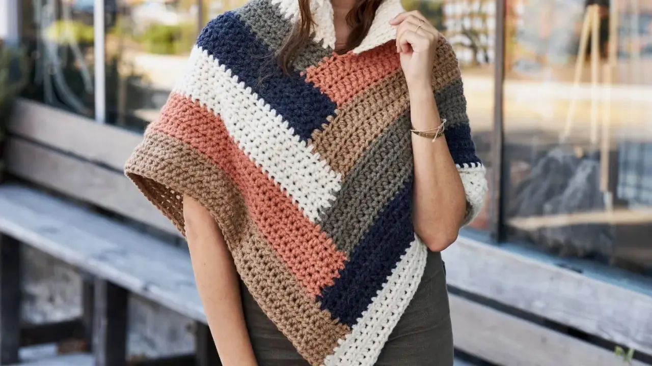 Mujer con un poncho de ganchillo a rayas en tonos tierra, azul marino y blanco. El patrón poncho es ideal para el otoño.