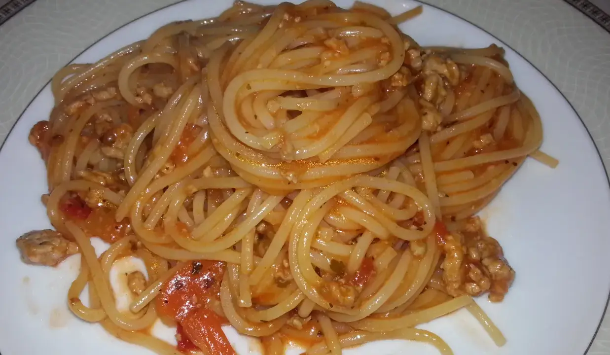 Pyszne spaghetti bolognese z passaty, z mielonym mięsem i kawałkami pomidorów, podane na białym talerzu.