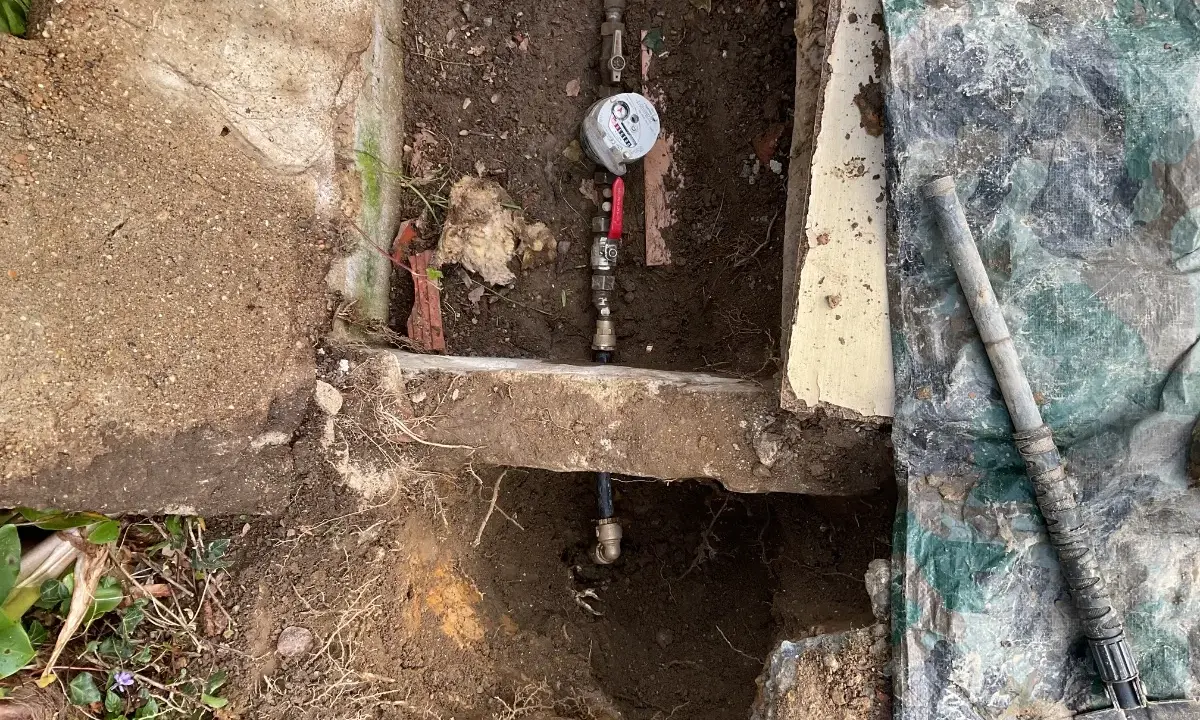 Réparation d'une fuite d'eau : un compteur et des tuyaux sont visibles dans une excavation, avec une bâche de protection à proximité.