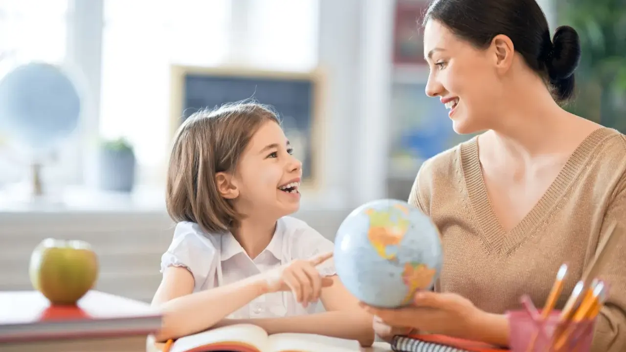 Niña y maestra sonríen mientras exploran un globo terráqueo. Un ejemplo de como ser un buen profesor, inspirando curiosidad y aprendizaje.