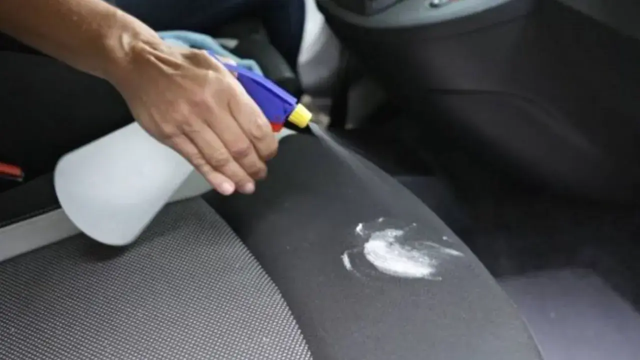 Mano rocía un asiento de coche con un limpiador para eliminar manchas de flujo.