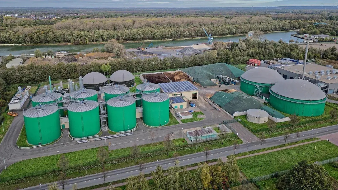 Grüne Biogas-Behälter und große Gasspeicher prägen diese Anlage, die die **Biogas Zukunft** symbolisiert. Im Hintergrund ein Fluss und bewaldete Ufer.