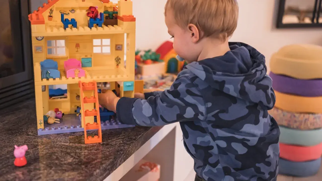 Kleiner Junge spielt mit einem Puppenhaus. Ein Schritt beim **Kinderzimmer ausmisten** ist, Spielzeug zu sortieren.