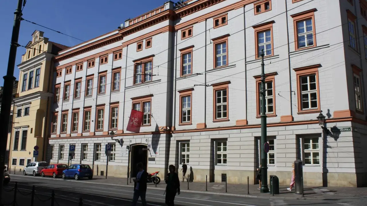 Uniwersytet Papieski w Krakowie, gdzie można studiować różne kierunki. Budynek z czerwonymi akcentami i flagą.