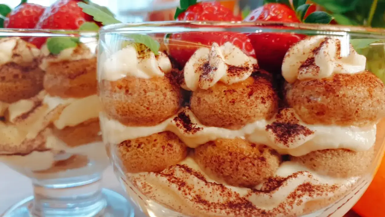 Pyszne tiramisu w pucharkach, przełożone kremem, biszkoptami i posypane kakao, ozdobione truskawkami i miętą.