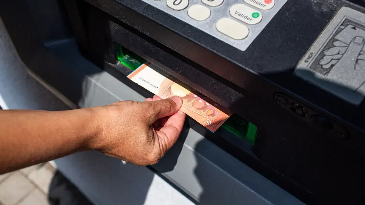 Mano sacando un billete de 50 euros de un cajero automático. La imagen muestra la acción de retirar dinero, lo que nos hace pensar en cuanto dinero se puede sacar del cajero.