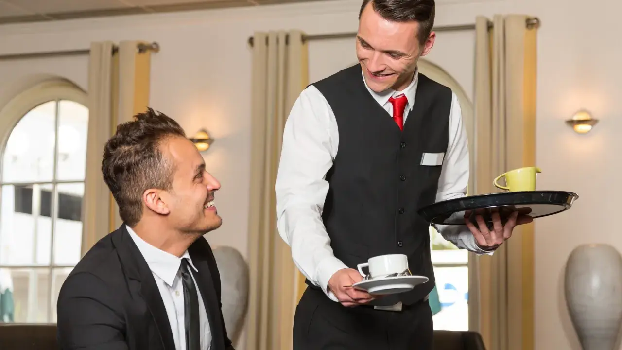 Un serveur souriant présente une tasse de café à un client, illustrant le protocole de service à table.