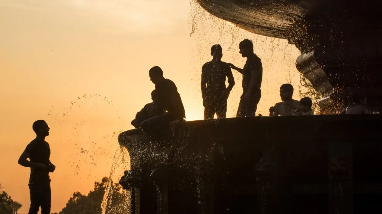 Silhouette fotografia di persone che si rinfrescano in una fontana al tramonto, con l'acqua che scintilla contro il cielo arancione.