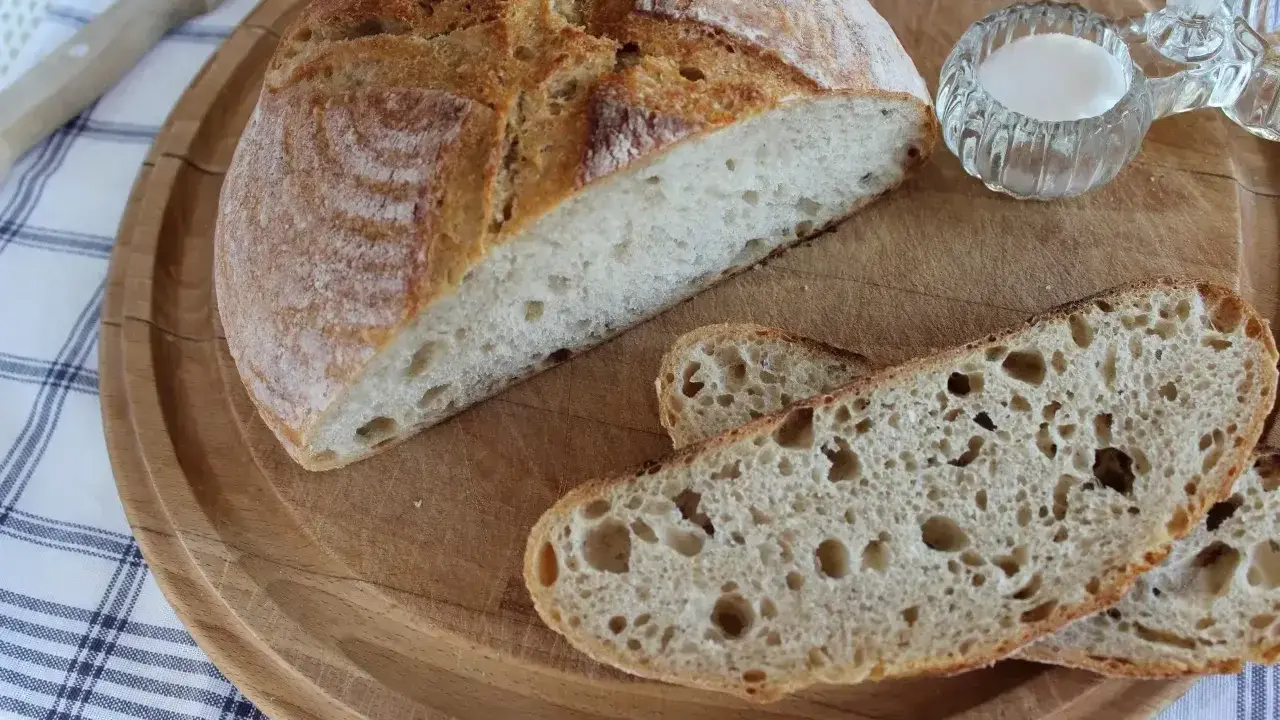 Chleb pszenny na zakwasie, pokrojony na desce, z solniczką i nożem w tle. Idealny na śniadanie.