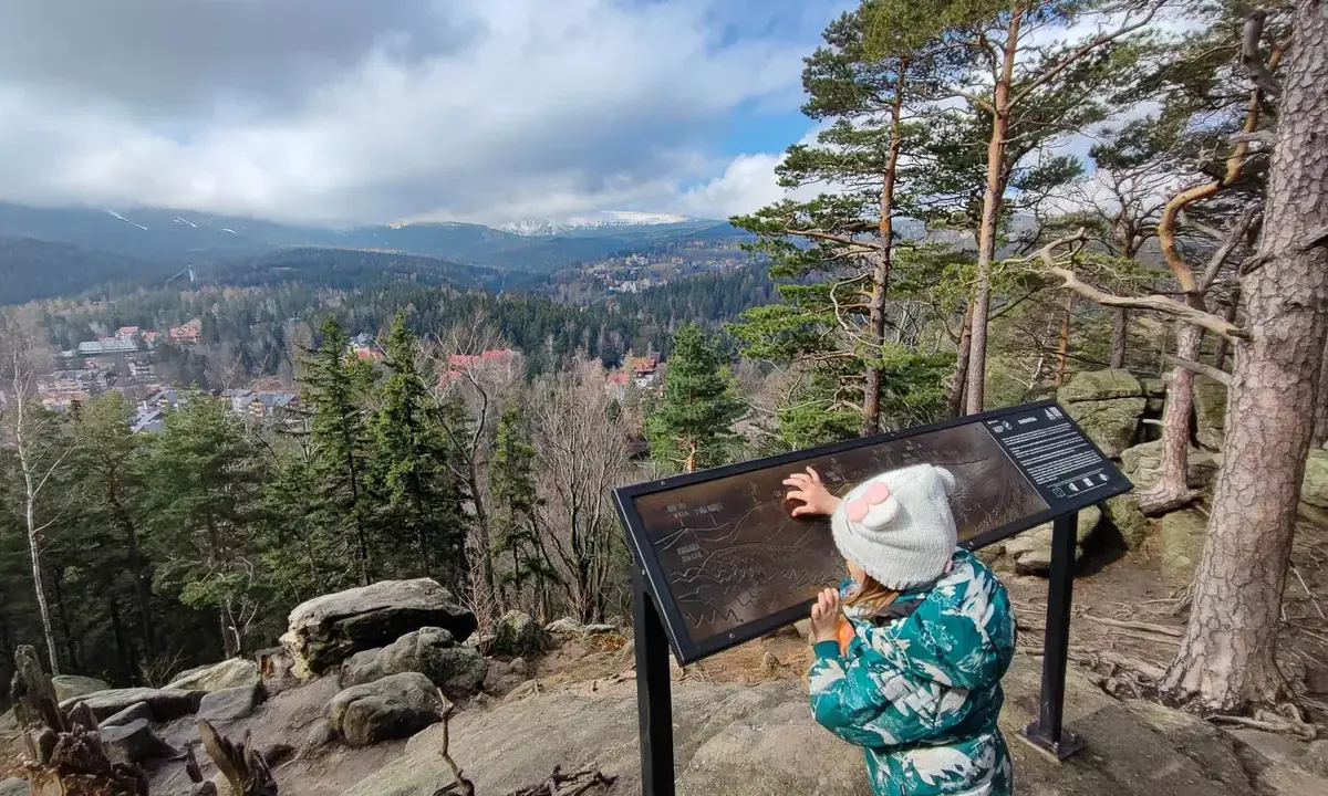Dziecko przy tablicy informacyjnej na punkcie widokowym Karpatka, podziwiające panoramę gór.