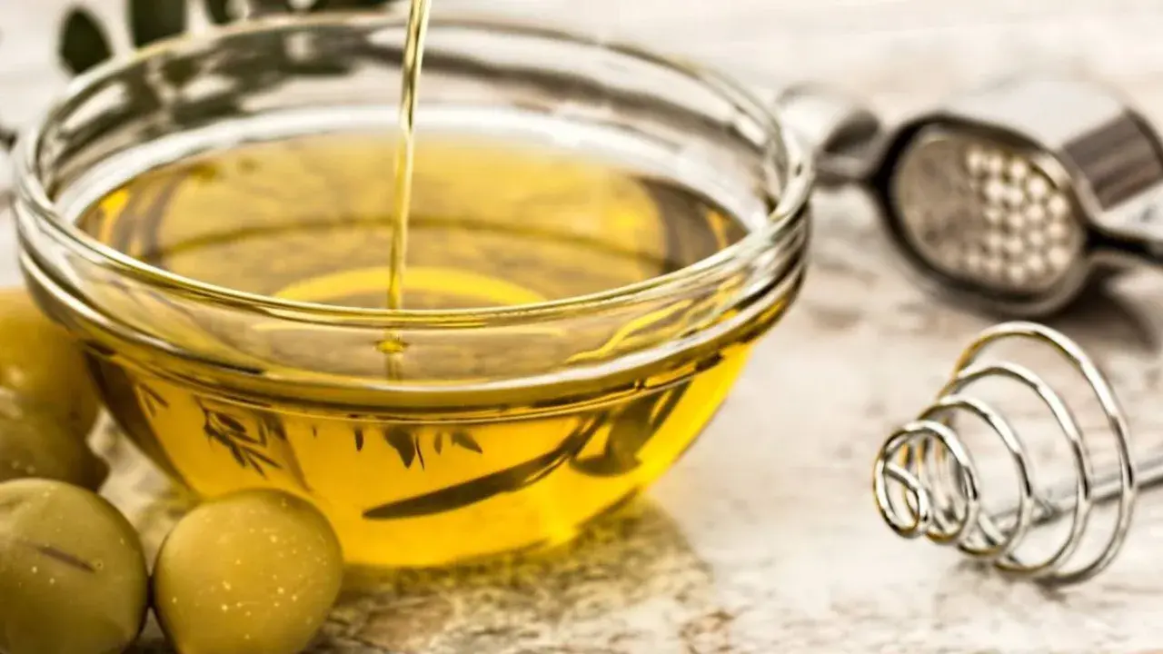 Aceite de oliva vertiéndose en un bol de cristal, rodeado de aceitunas. Varios tipos de aceite comestible para cocinar.