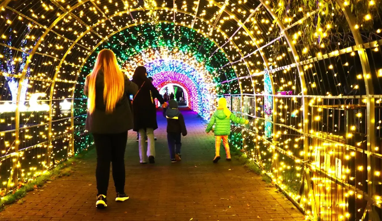 Rodzina spaceruje przez świetlisty tunel w Krakowie. Kolorowe lampki tworzą magiczny ogród świateł.
