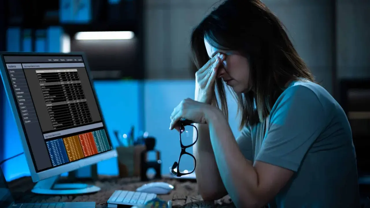 Femme fatiguée devant un écran, lunettes à la main. La hyperconnectivité définition se reflète dans son regard las face aux données.
