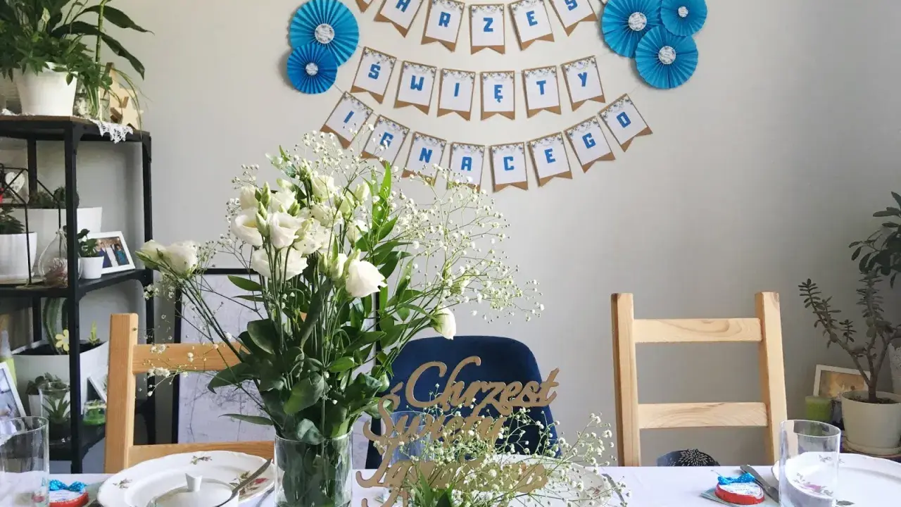 Urocze dekoracje na chrzest diy: girlanda "Chrzest Święty", bukiety białych kwiatów i ozdobne napisy.