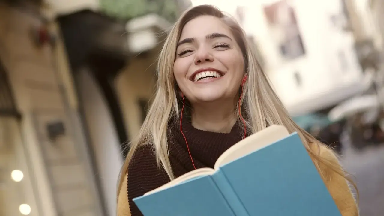 Uśmiechnięta dziewczyna z książką i słuchawkami na ulicy. Może to być studentka, która właśnie skończyła lekcje w szkole w Danii.