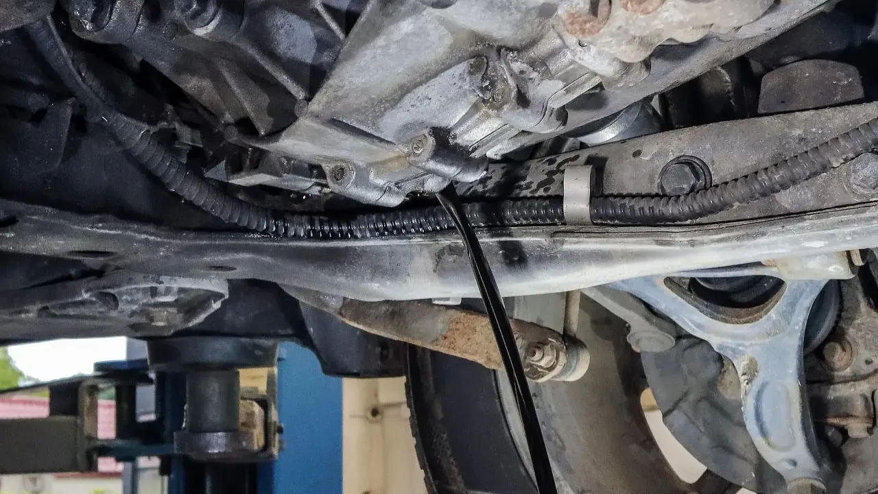 Wymiana oleju w skrzyni manualnej. Mechanik spuszcza stary olej z przekładni.
