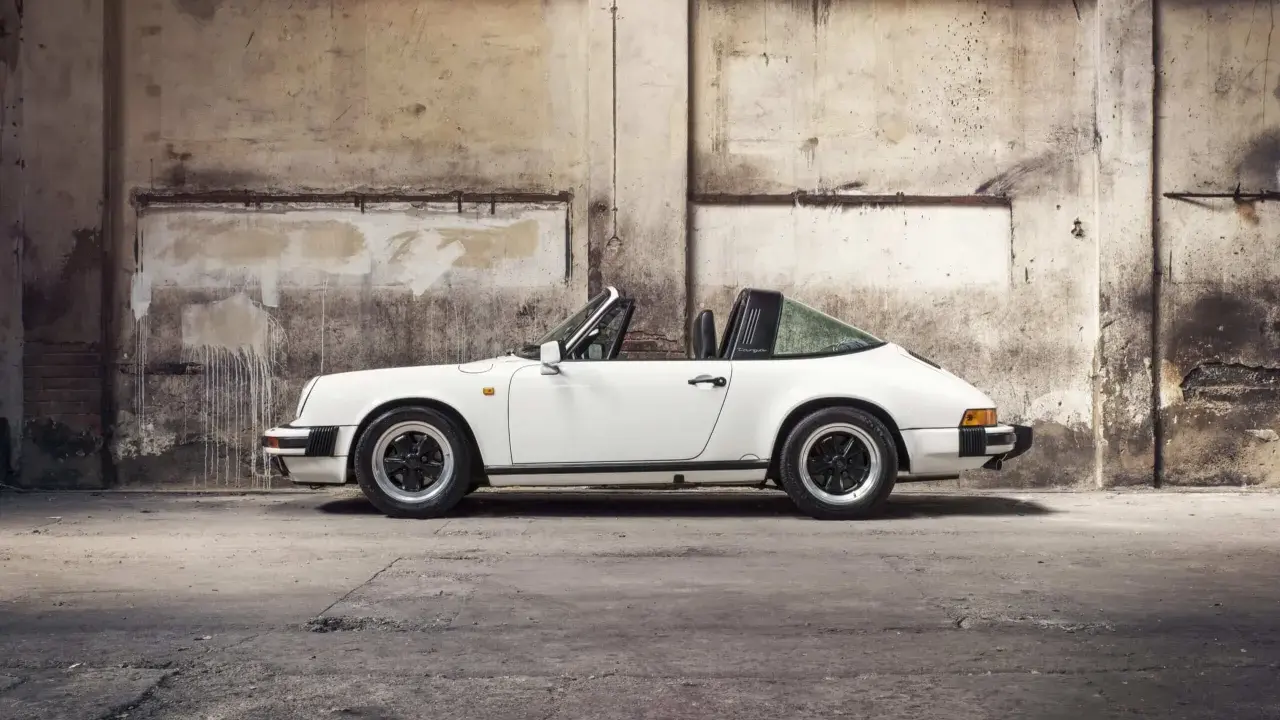 Weißer Porsche 911 3.2 Carrera Targa, ein Klassiker mit stabiler Wertentwicklung, steht in einer alten Lagerhalle.