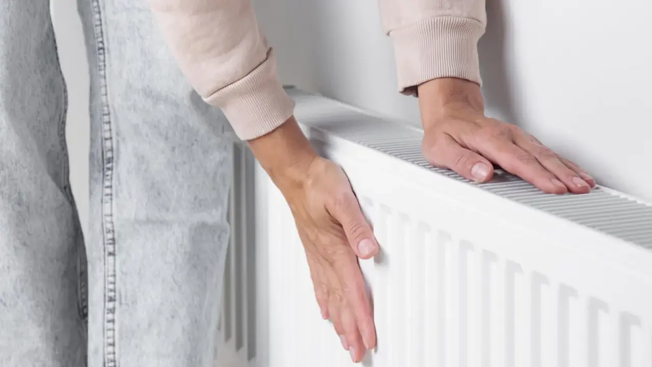 Dłonie sprawdzają temperaturę grzejnika, który słabo grzeje. Zimno w domu, trzeba coś z tym zrobić.