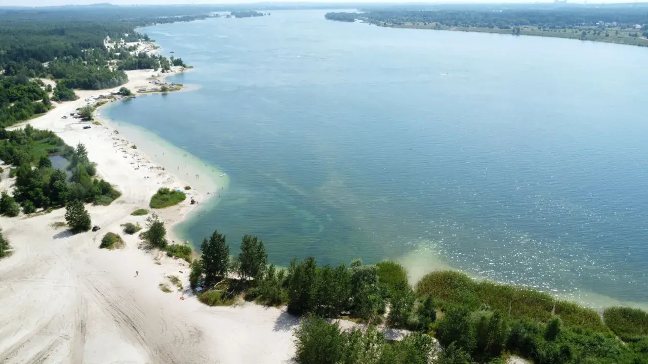 Plaża nad jeziorem, piasek, drzewa i ludzie odpoczywający w słońcu. Idealne miejsce na wakacje, jak z **pogoria** 1.