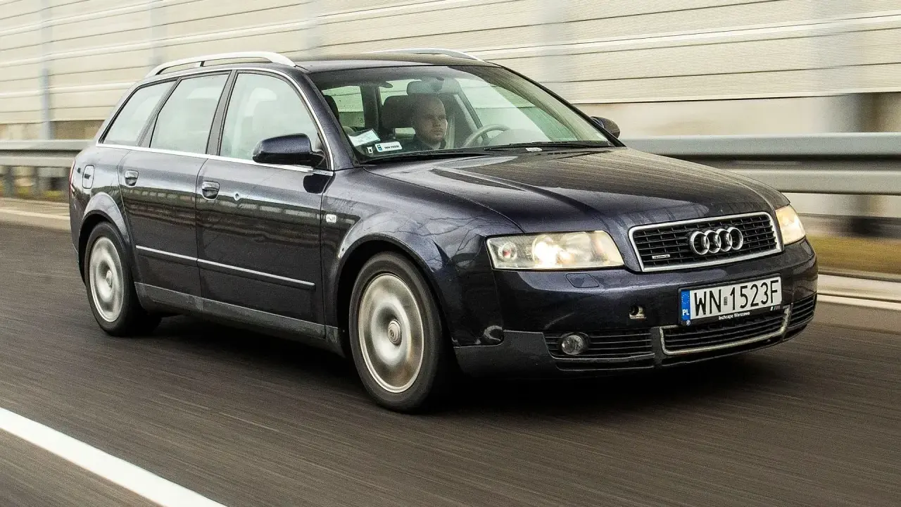 Ciemnogranatowe Audi A4 B6 2.0 Avant pędzi autostradą. Kierowca skupiony na drodze.