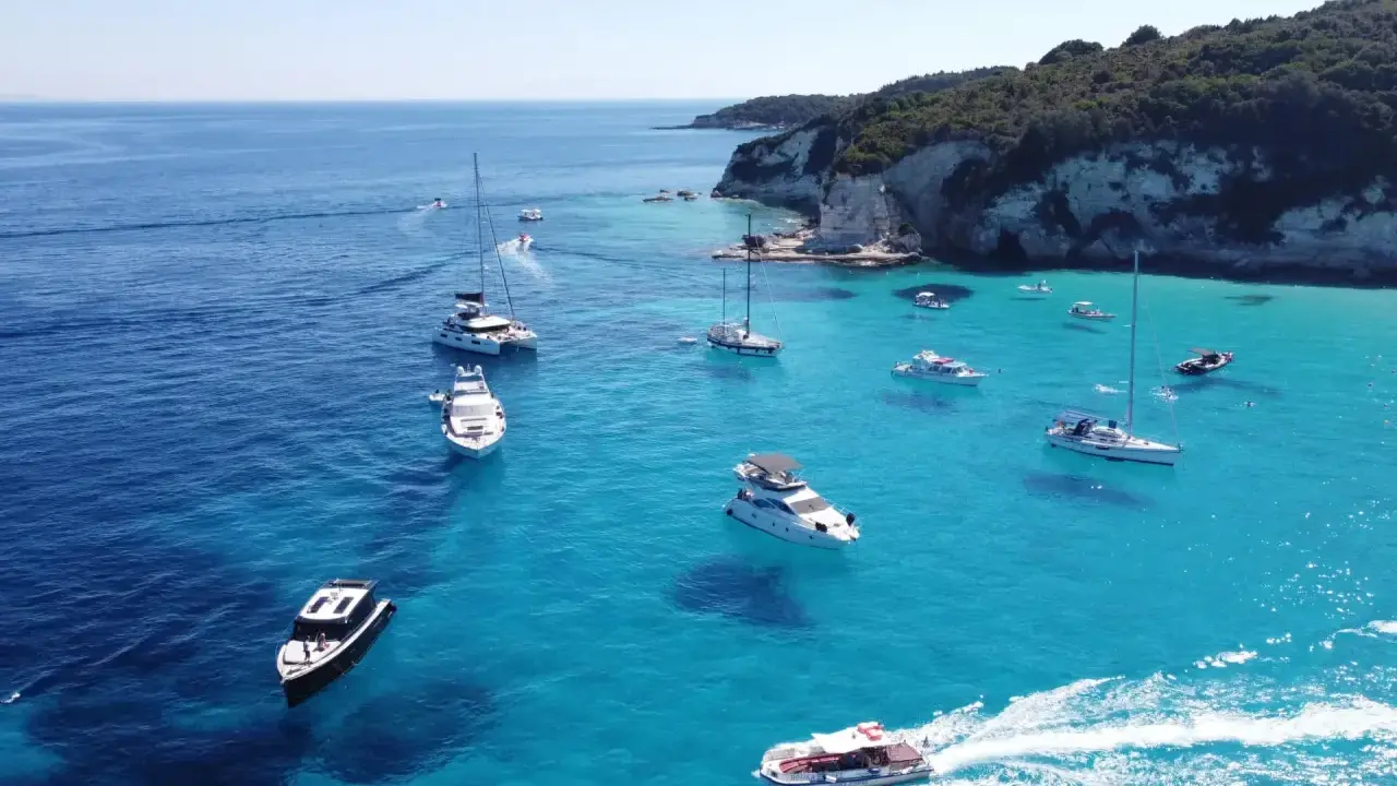 Båtar i turkost vatten vid en klippig kust, en idyllisk vy från Paxos, Grekland.